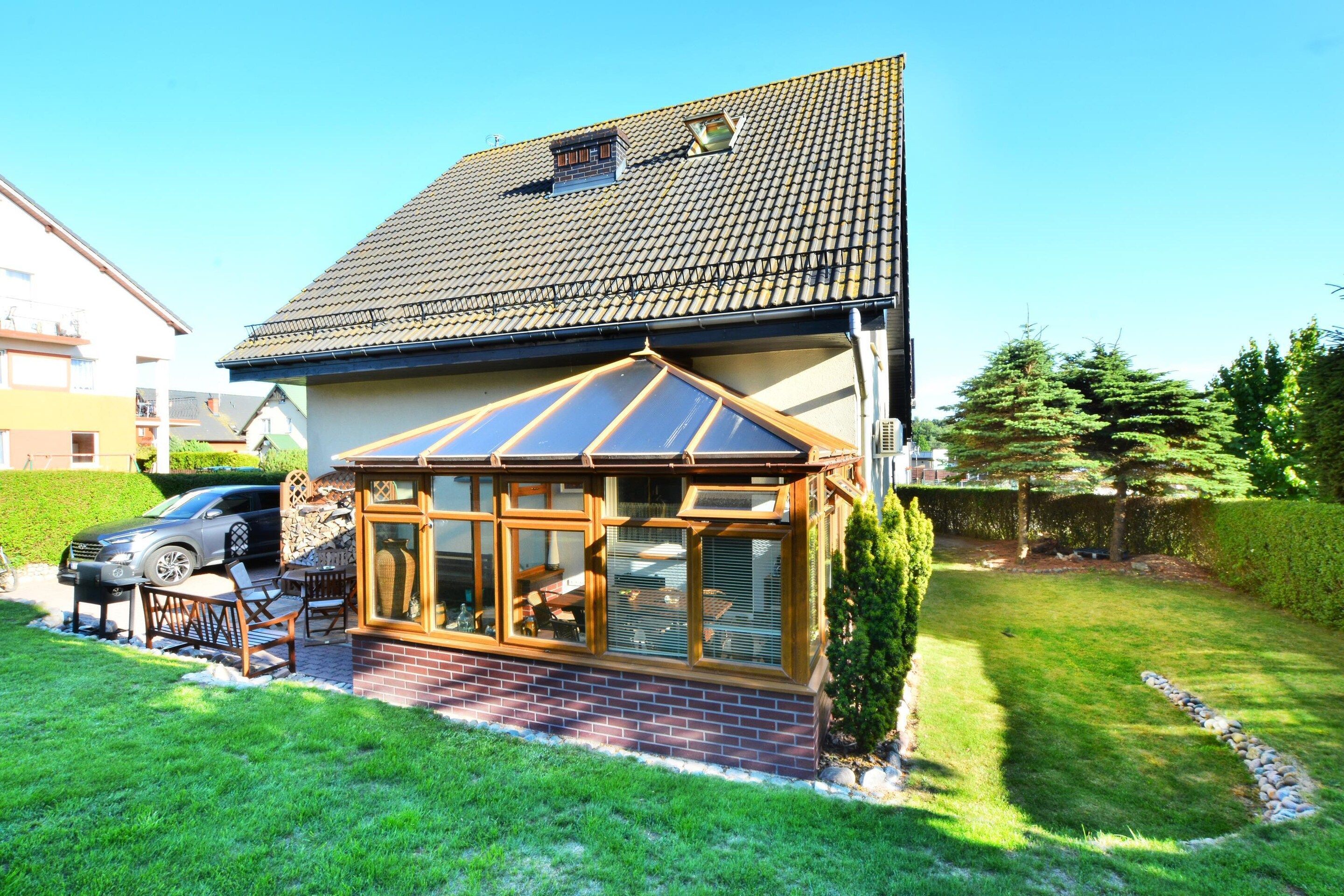 A house with a conservatory, a car parked in the driveway, and a well-maintained lawn.