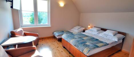 A bedroom with a large bed, a small table, and two chairs. There is a window providing natural light.
