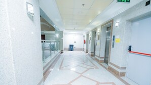 A clean, well-lit hallway with a geometric floor pattern, glass railings, and an elevator. - Asfour Hotel 03 (Makkah)