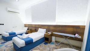 A hotel room with two beds, a wooden headboard, a small table, an ironing board, and a wall-mounted air conditioner. - Asfour Hotel 03 (Makkah)