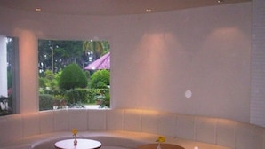 Un espace salon moderne aux lignes courbes, avec deux tables rondes, une grande fenêtre offrant une vue sur la verdure et un bâtiment, et un design épuré et minimaliste.
