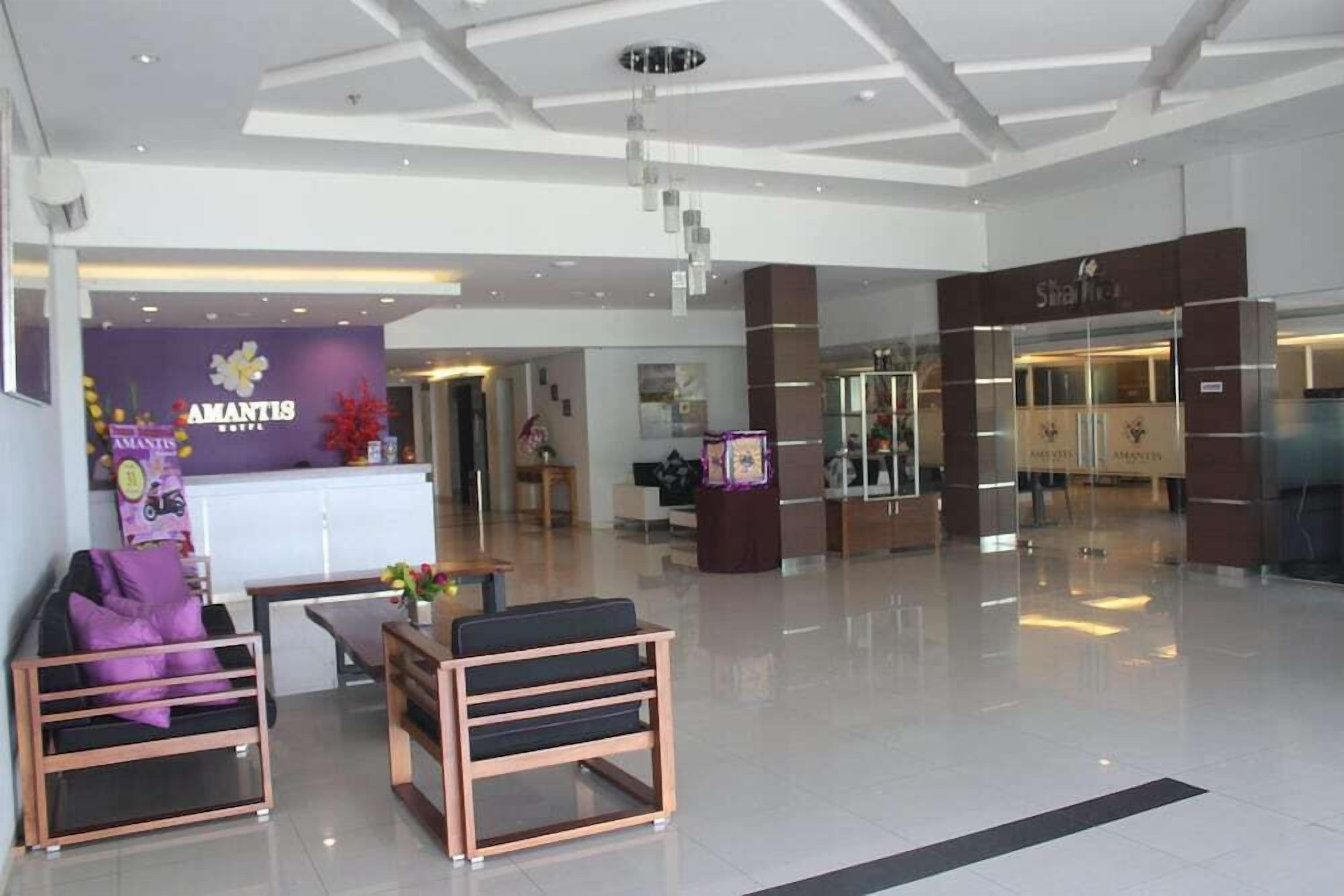 A modern hotel lobby with a reception desk, seating area, and a staircase leading to other floors.