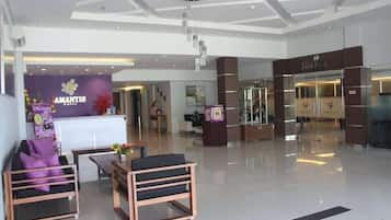 A modern hotel lobby with a reception desk, seating area, and a staircase leading to other floors.