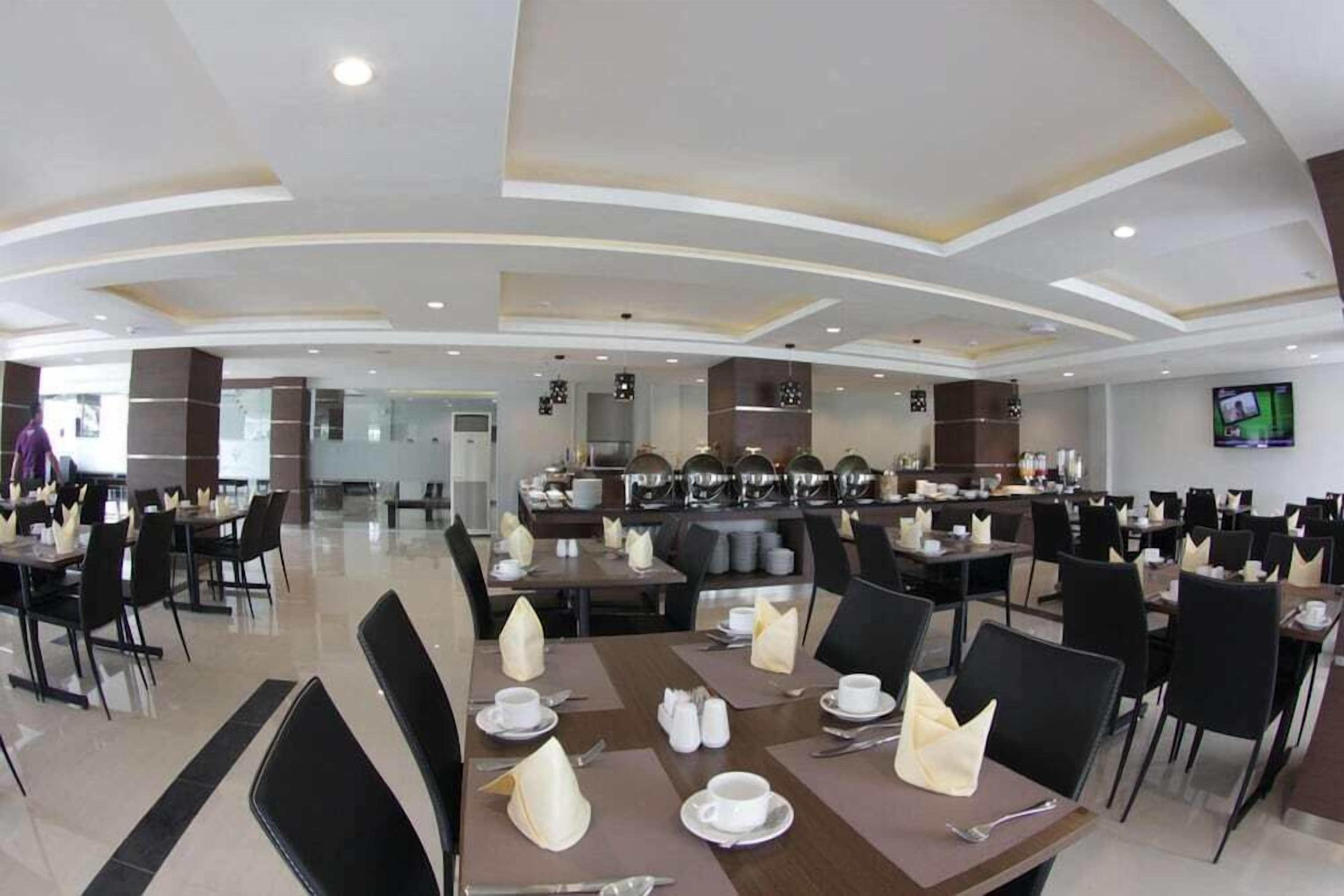 A spacious dining area with multiple tables and chairs, a central buffet, and a television screen on the wall.