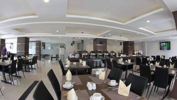 A spacious dining area with multiple tables and chairs, a central buffet, and a television screen on the wall.