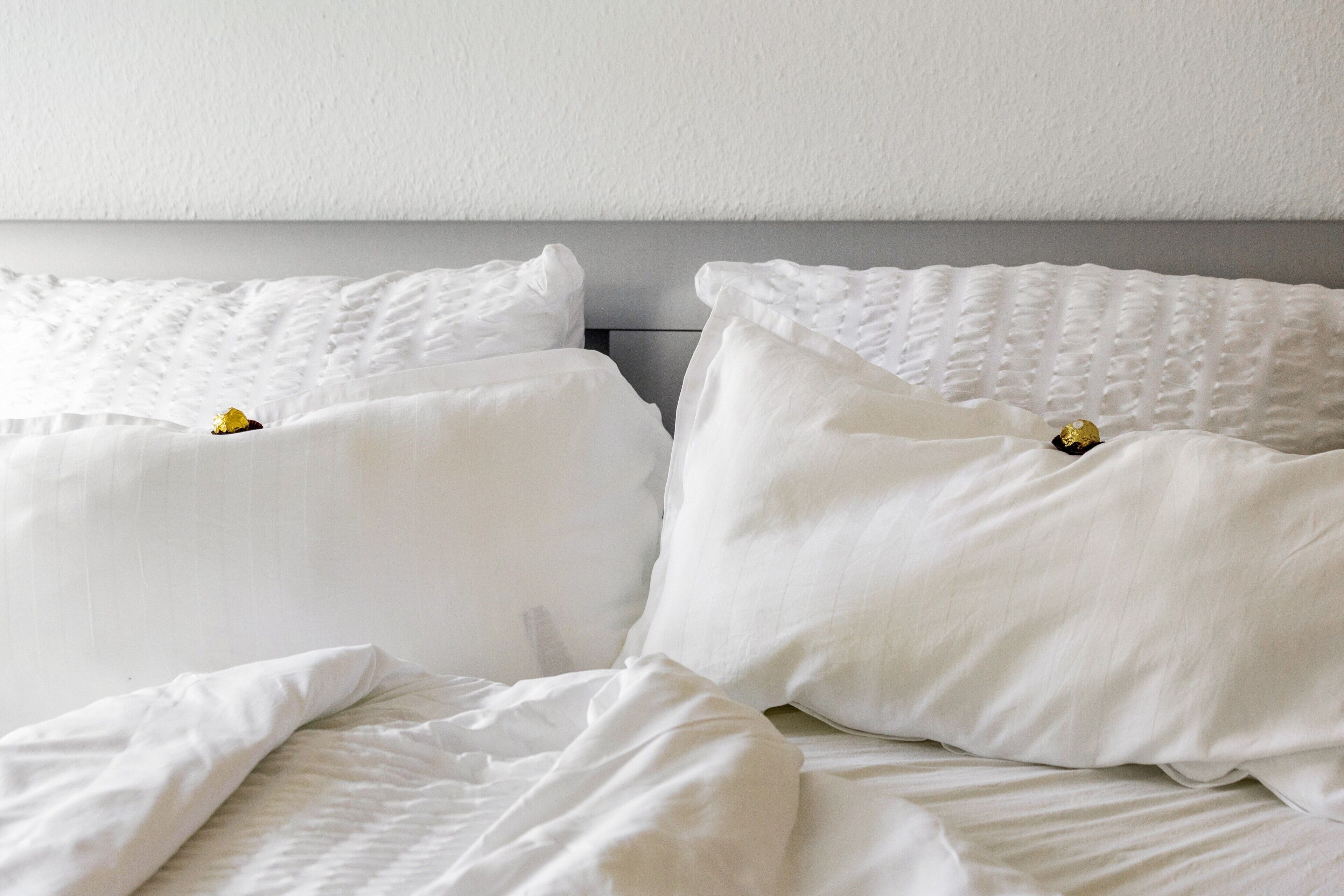 Ein Bett mit weißer Bettwäsche und Kissen, ein grauer Kopfteil und eine schlichte Wand.