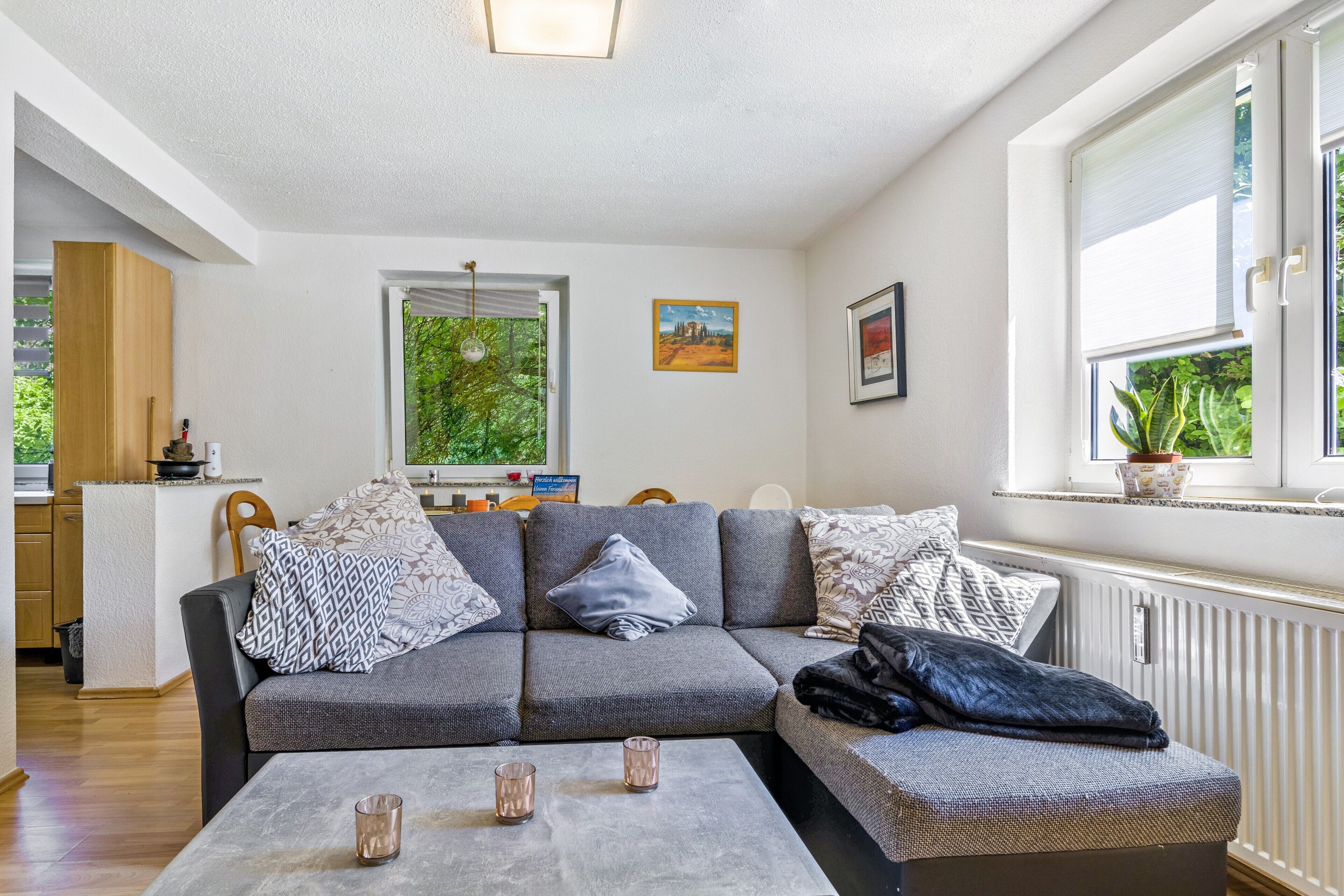 A modern living room with a grey sofa, a coffee table, and a window with a view of greenery.