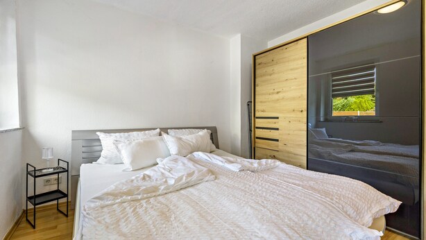 A bedroom with a bed, a bedside table, a wardrobe, and a window. - Apartment 'Ferienwohnung' with Wi-Fi (Recklinghausen)