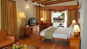 A hotel room with a bed, a sofa, a television, a desk, and a window with curtains. - Lemon Tree Vembanad Lake Resort Muhamma (Cherthala)