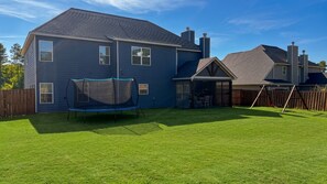 A residential backyard with a trampoline, a wooden fence, and a covered patio area. - Peaceful spacious 4-bedroom Kid-Friendly 2026 Master's Retreat. (Evans)