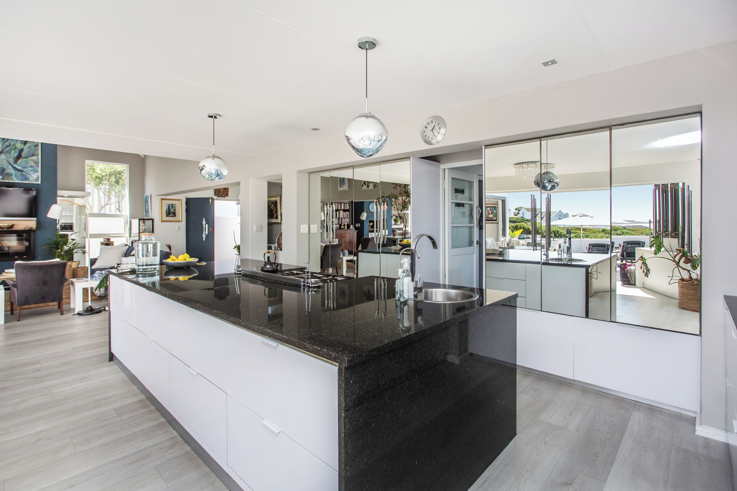 A modern kitchen with a large island, white cabinetry, and a view of the outdoors through a glass door.