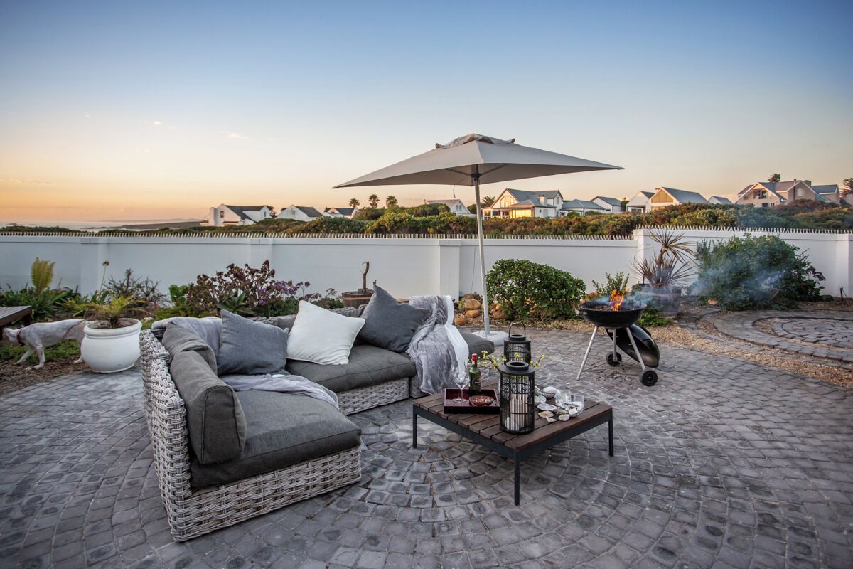 A patio with a wicker sofa, a table with drinks, and a grill.