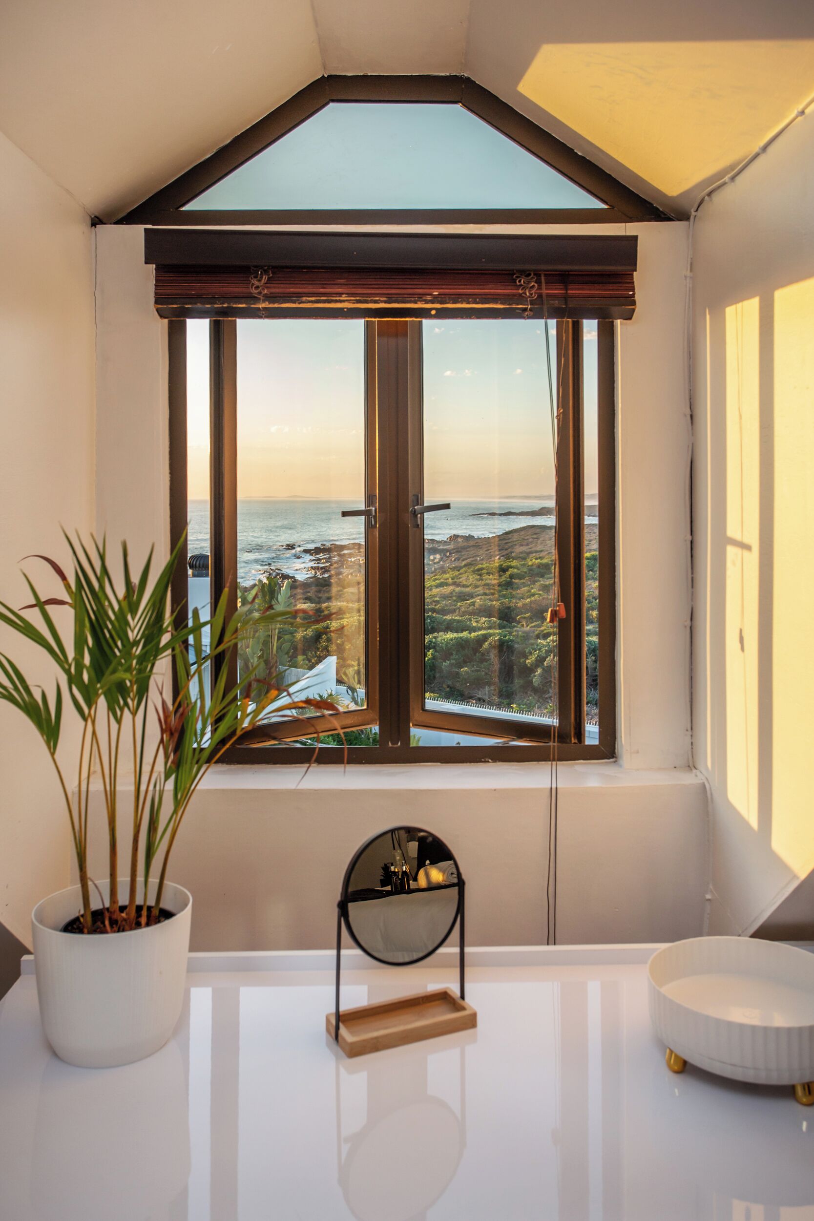 A modern bathroom with a skylight, a potted plant, a round mirror, and a bathtub.
