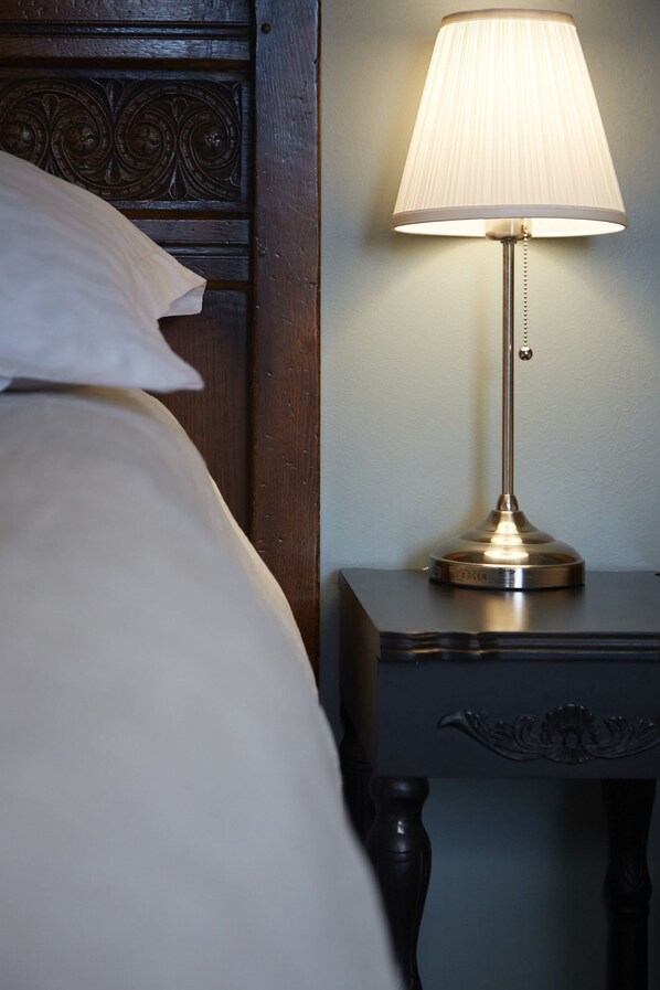 A neatly made bed with a white pillow, a wooden headboard with carved designs, and a bedside table with a lamp. - Hrafninn Guesthouse (Akureyri)