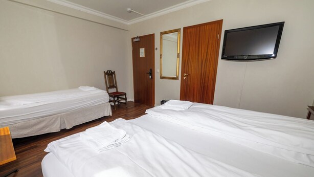 Een hotelkamer met twee enkele bedden, een houten stoel, een televisie en een spiegel aan de muur.