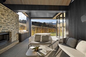 Un espace de vie extérieur moderne, agrémenté d’un mur en pierre, d’une cheminée intégrée, d’un coin salon avec une table et offrant une vue sur un paysage vallonné.