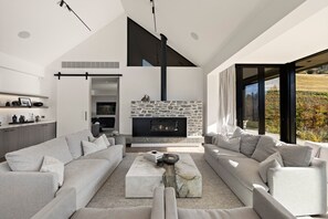 A modern living room with a stone fireplace, a large sectional sofa, and a minimalist design. - The Paddock by MajorDomo | Stunning Rural Property with Spa Pool (Queenstown)