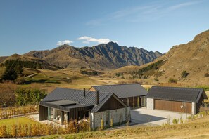 A modern house with a stone facade and a metal roof, set against a mountainous backdrop. - The Paddock by MajorDomo | Stunning Rural Property with Spa Pool (Queenstown)