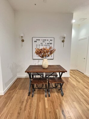 Ein Essbereich mit einem Holztisch und Bänken, einer Vase mit getrockneten Blumen und einem gerahmten Bild an der Wand.