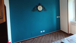Ein Zimmer mit einer türkisfarbenen Wand, einer Zieruhr, einem Holzboden und einem Fenster mit Blick.