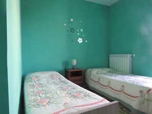Habitació amb dos llits, parets color turquesa, un radiador i una nitòria amb una làmpada.