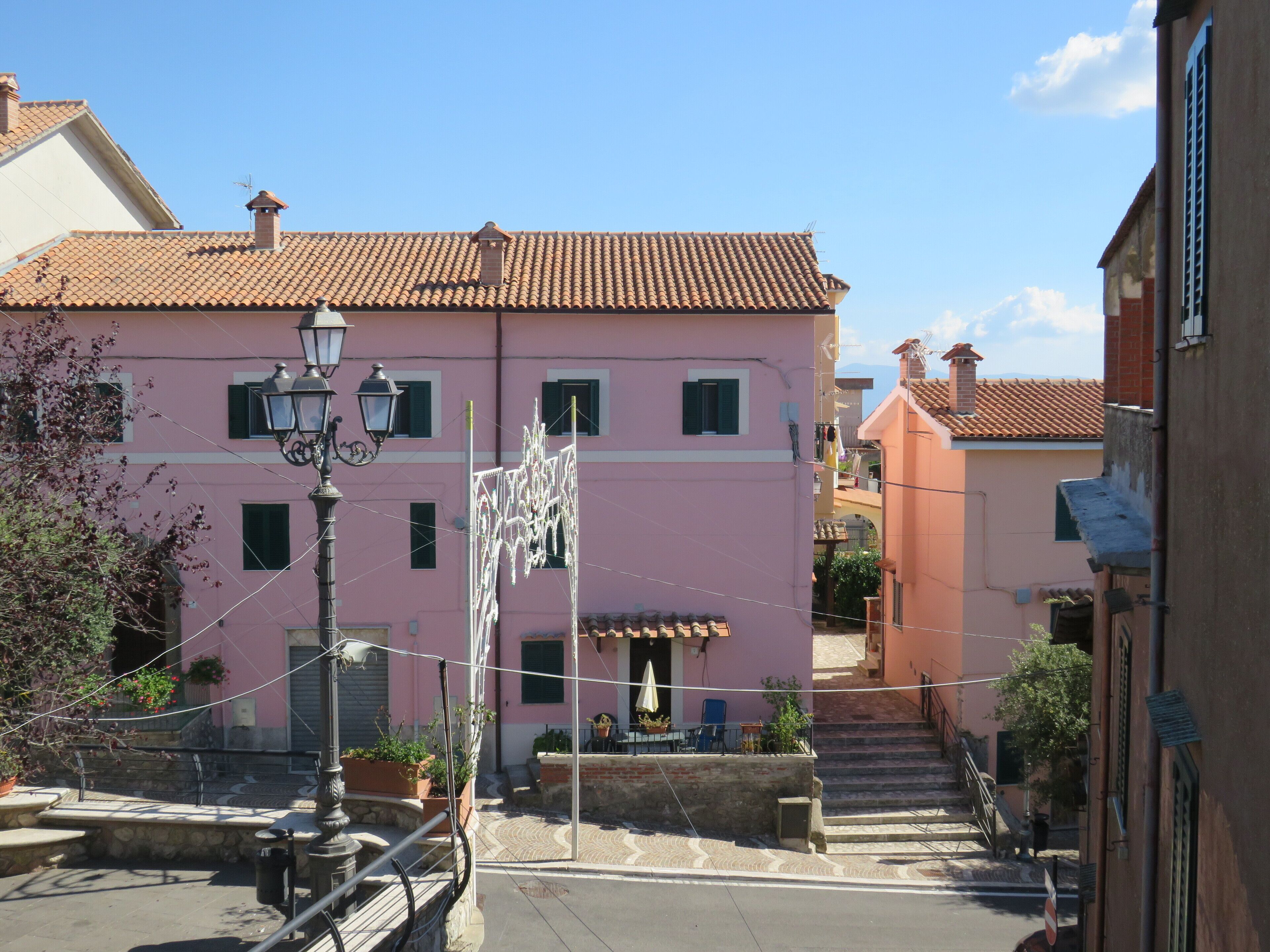 A pink building with a tiled roof, a street lamp, and a staircase leading to a second floor.