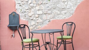 Un petit espace extérieur aménagé avec deux chaises en métal et une table, le tout adossé à un mur rose à la texture pierre.