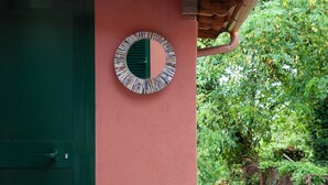 Une porte verte ornée d’un miroir rond, le tout adossé à un mur rose et entouré de verdure.