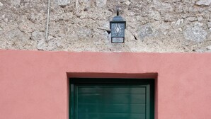 Une porte verte, précédée d’un petit marchepied, est encadrée dans un mur rose dont la base est en pierre.