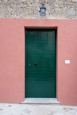 Eine grüne Tür mit einer kleinen Stufe, eingebettet in eine rosa Wand mit steinernen Fundament.