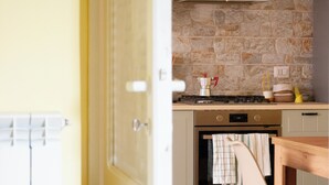 Une cuisine avec un mur recouvert de pierres derrière l’évier, une cuisinière et une table à manger en bois avec une chaise.