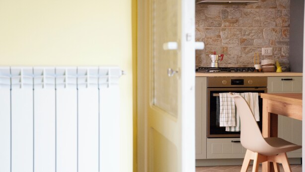 Une cuisine avec un mur en pierre, une cuisinière, un four et une table en bois accompagnée d’une chaise.