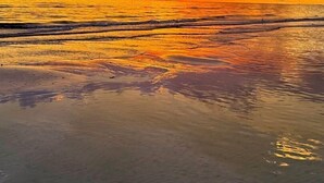 Ein Strand mit Sonnenuntergang, ruhigem Wasser und klarem Himmel.