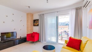 A modern living room with a flat-screen TV, a red chair, a yellow sofa, and a balcony with a mountain view. - Newly decorated apartment in a quiet part of Baška (Baška)
