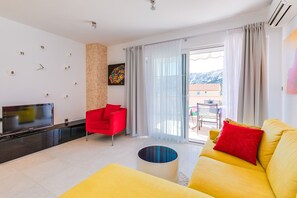 A modern living room with a flat-screen TV, a red chair, a yellow sofa, and a balcony with a mountain view. - Newly decorated apartment in a quiet part of Baška (Baška)