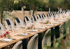 A long dining table set outdoors with wicker chairs, clear glassware, and floral centerpieces. - Rancho Pescadero (El Pescadero)