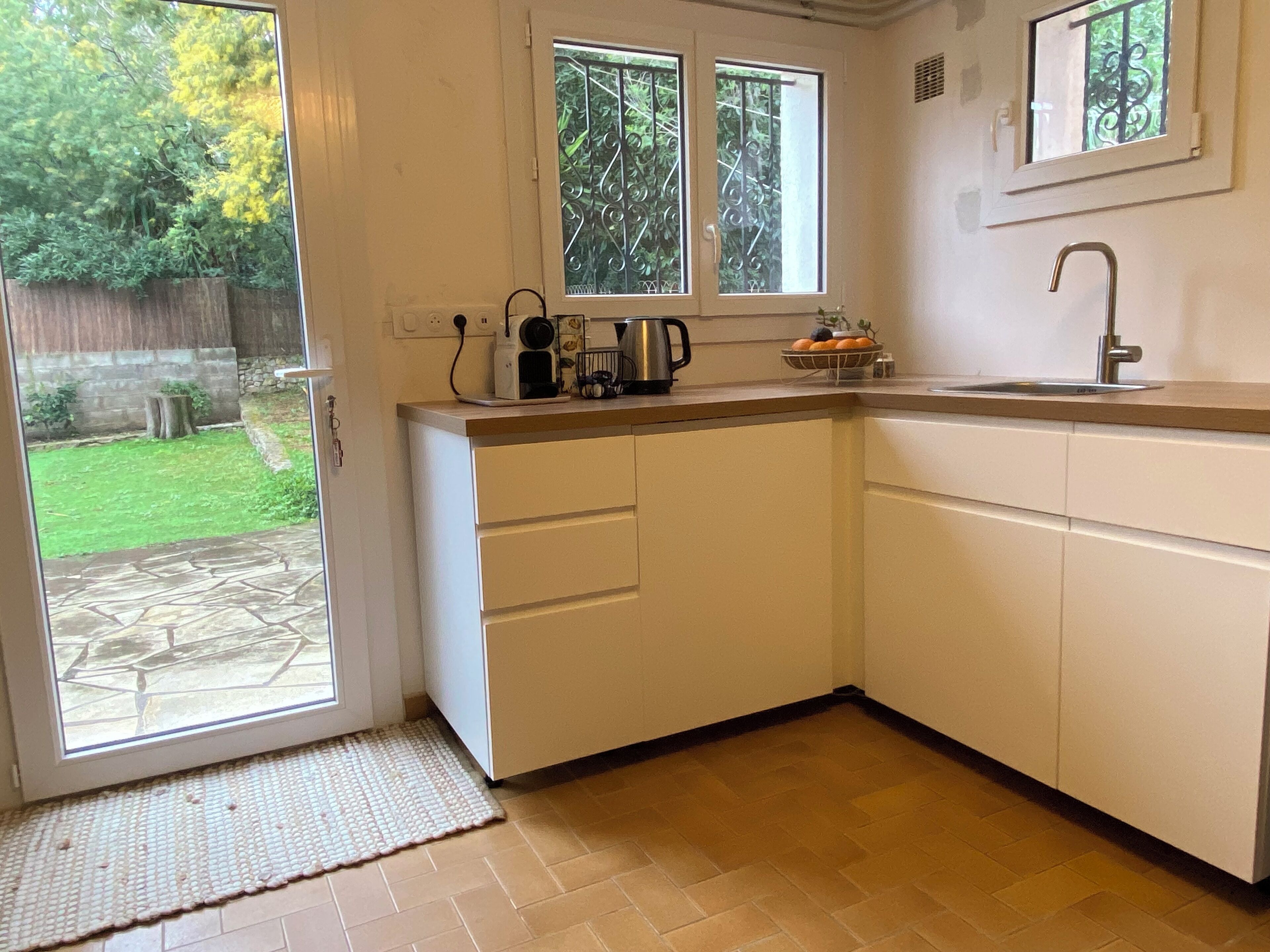 A kitchen with white cabinets, a countertop, a sink, and a window overlooking a garden.