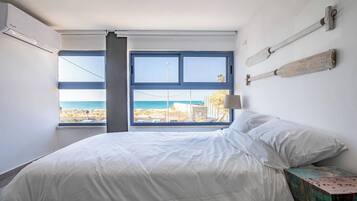 Un dormitorio con cama, ventana con vista a la playa y una lámpara fijada a la pared.