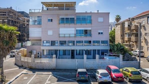 A multi-story building with a flat roof, large windows, and a parking lot with several cars. - Port city haifa- beachfront complex (Haifa)