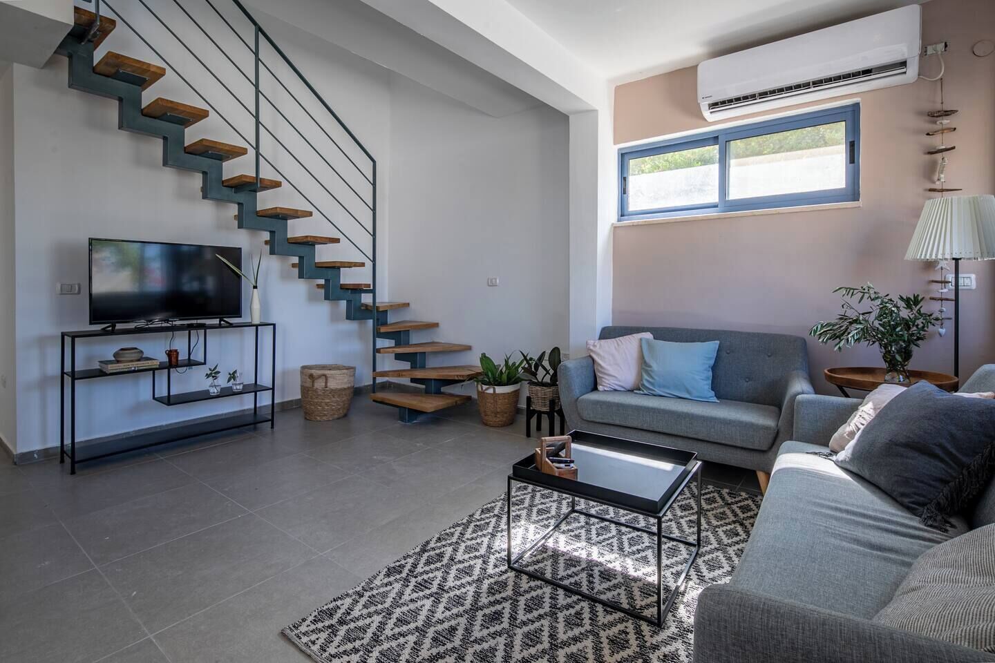 Una sala de estar moderna con una escalera, un televisor de pantalla plana, un sofá y una mesita de centro.
