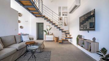 Un salon moderne avec un escalier, un canapé, une table basse et un téléviseur fixé au mur.