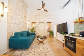 Uma sala de estar com um sofá verde-água, uma mesa de centro, uma TV e uma cozinha com fogão.