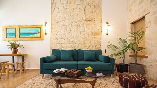 Un soggiorno con un divano color petrolio, un tavolino da caffè, un tappeto decorato, un muro in pietra e un quadro appeso.