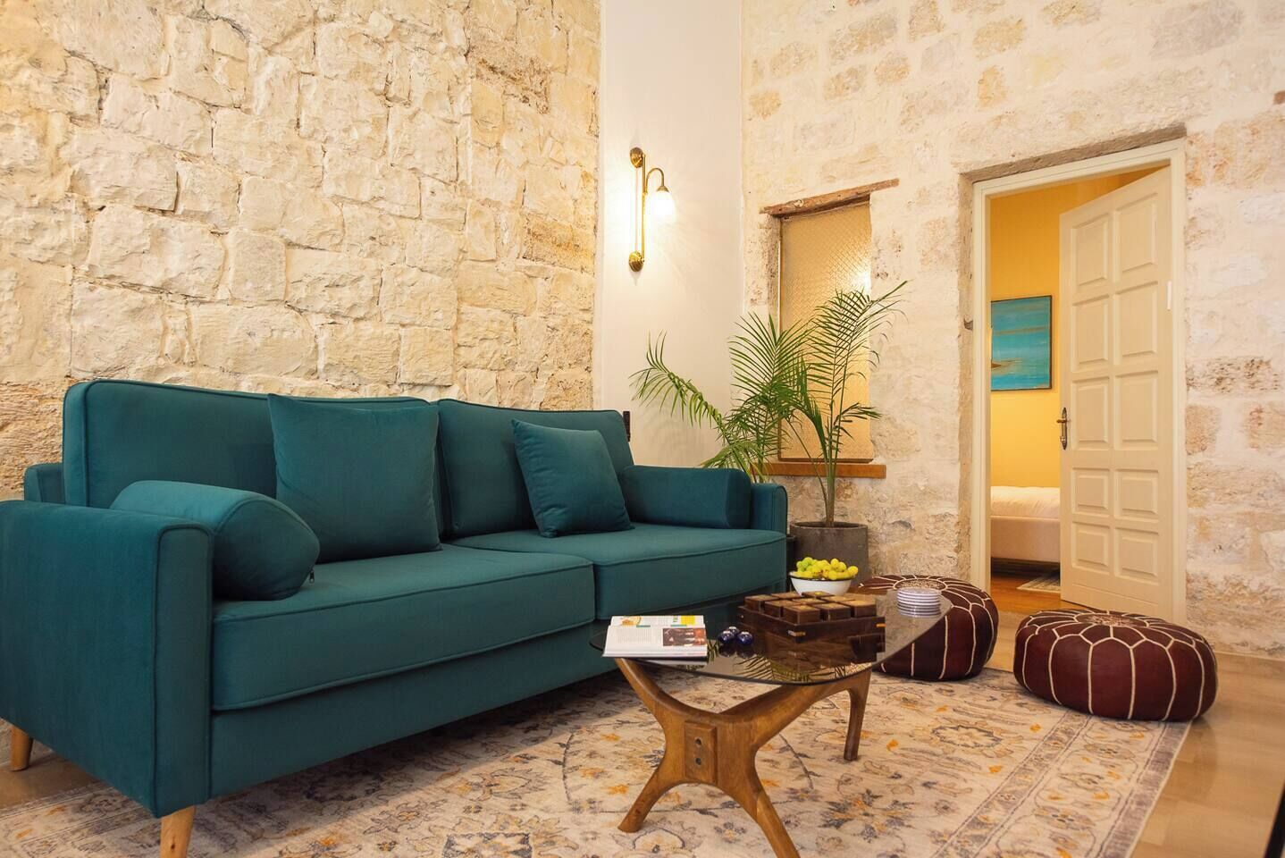 A cozy living room with a teal sofa, a coffee table, and a stone wall.