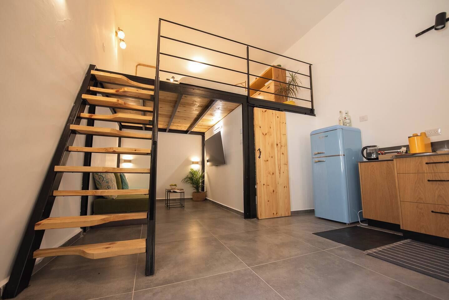 Una cocina moderna con un refrigerador azul, armarios de madera y una escalera con barandilla negra.