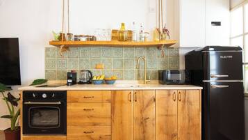 A kitchen with a black refrigerator, a coffee maker, a microwave, and a wooden cabinet with drawers.