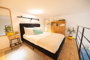 A bedroom with a bed, bedside table, lamp, wardrobe, and a potted plant.