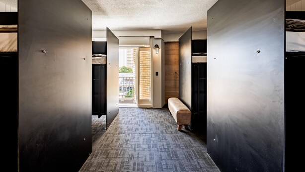 A modern hotel corridor with a bench, a door leading to a balcony, and a view of the outside. - Bunk Backpackers Surfers Paradise Hostel (Gold Coast)
