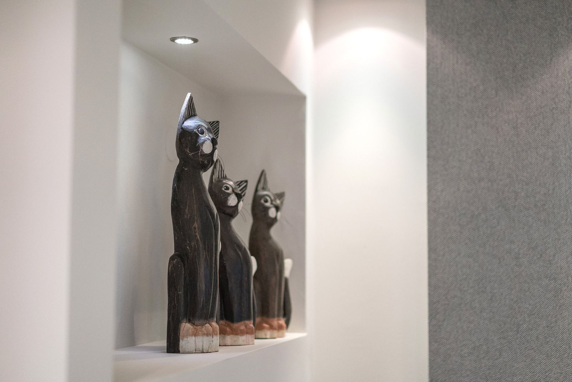 Una exposición de tres figuras de gatos sobre una estantería.