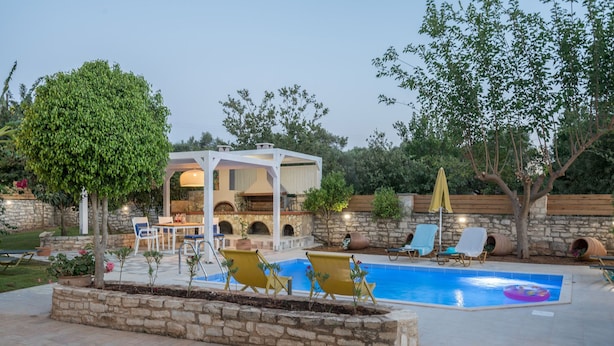 Un espace piscine comprenant des chaises longues, une pergola et un mur en pierre.
